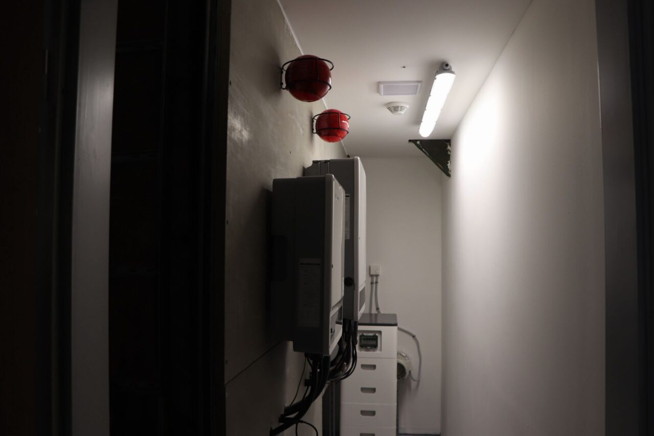 Servisní místnost k fotovoltaice Lindab se nachází na půdě kulturního domu, bezpečnost zabezpečují červené kulaté hasicí přístroje. Foto: Karolína Chlumecká, Ekonews